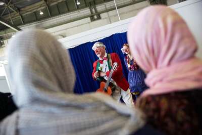 Ein Clown spielt vor einer Gruppe vor Frauen Gittare