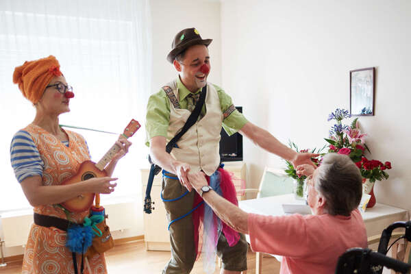 Zwei Clowns besuchen eine ältere Dame auf ihrem Zimmer im Pflegeheim