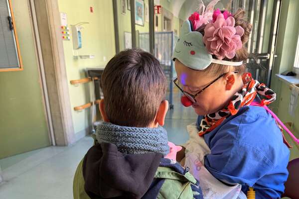 Ein Clown im blauen Kittel sitzt und ein kleiner Junge schaut ihn an.