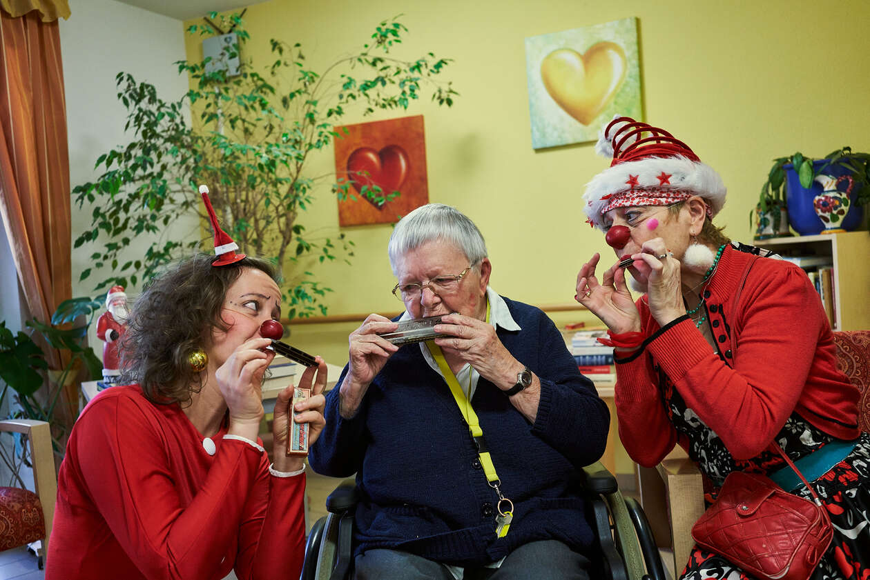 zwei weihnachtlich gekleidete Clowns sitzen neben einer älteren Dame und machen gemeinsam Musik