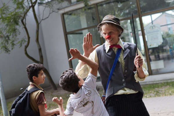 Der Clown Filou gibt einem Jungen in einem Flüchtlingheim einen Handschlag 