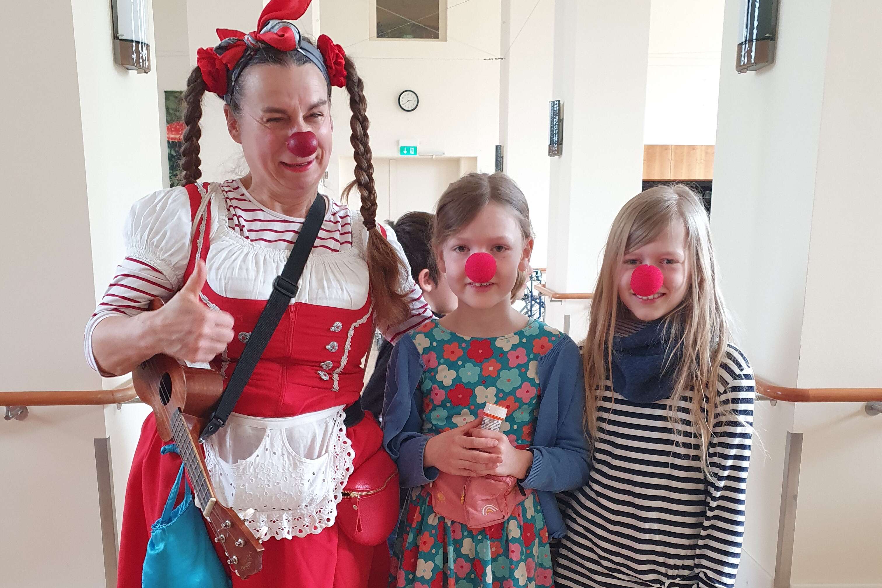 Ein Clown mit zwei Mädchen, die ebenfalls rote Nasen tragen lächeln in die Kamera.