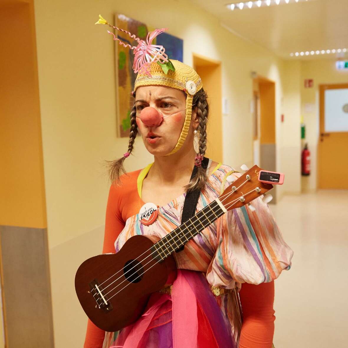 Clown Friedel steht mit Ukulele im Flur einer Klinik