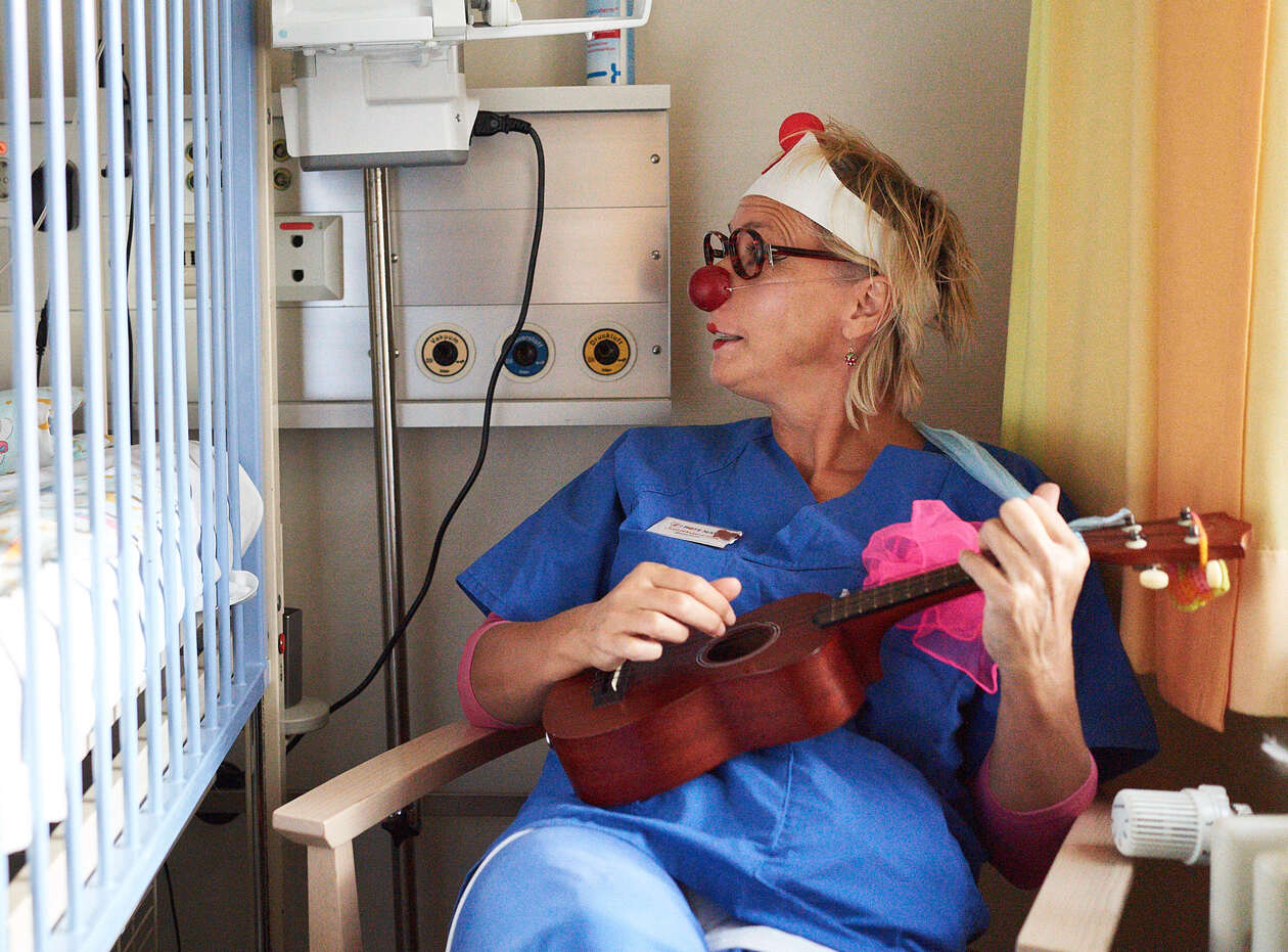 ein Clown mit einer Ukulele sitzt auf einem Stuhl in einem Krankenhaus