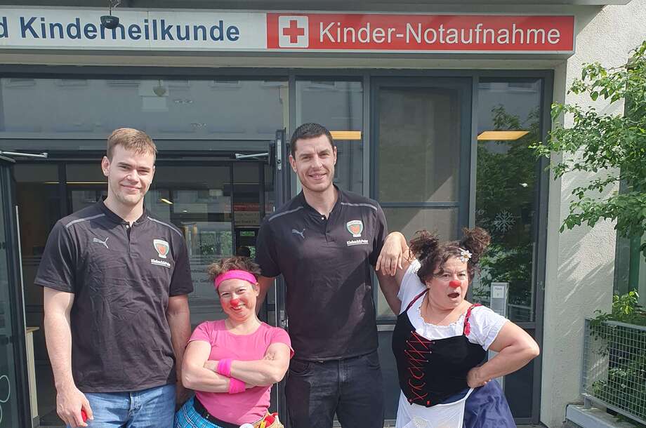 Zwei Handballspieler stehen mit zwei Clowns vor dem Eingang zur Notaufnahme des Klinikums Ernst von Bergmann.