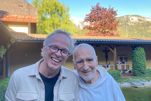 Reinhard Horstkotte und Benediktinermönch Bruder David Steindl-Rast umarmen sich und lächeln in die Kamera. 