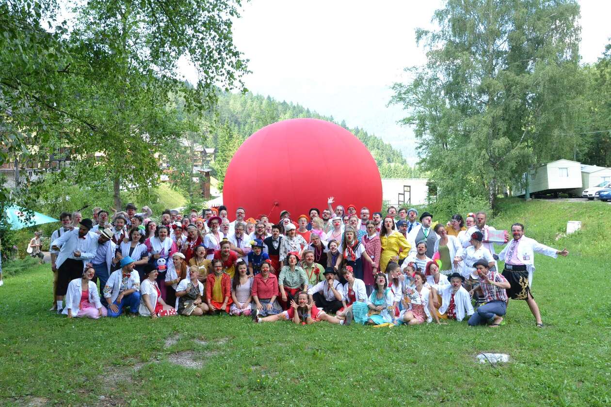 Ein Gruppen Bild mit allen Künstlern und Workshop leitern vor einem risen roten Luftballon auf einer Wiese