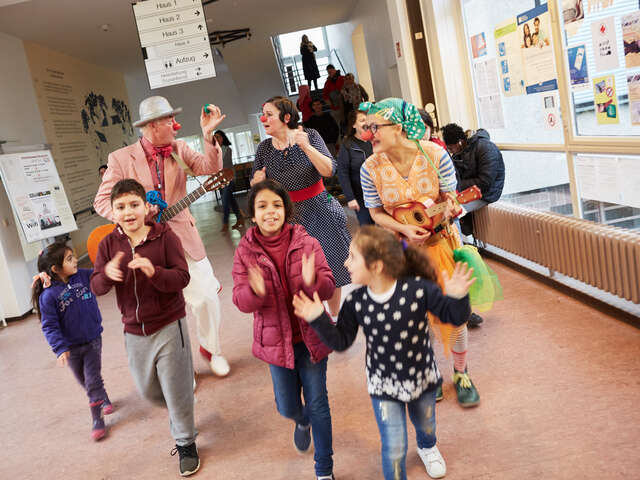 Die Clowns hüpfen fröhlich mit den Kindern durch die Fluchtlingsunterkunft 