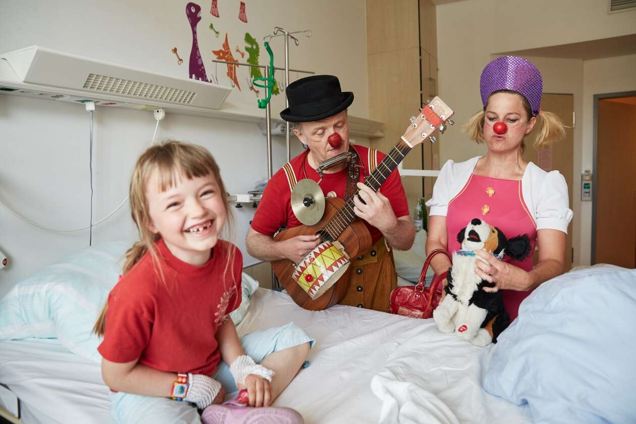 Ein Mädchen lacht sich in ihrem Krankenhausbett kaputt über die Nummer der Klinikclowns 