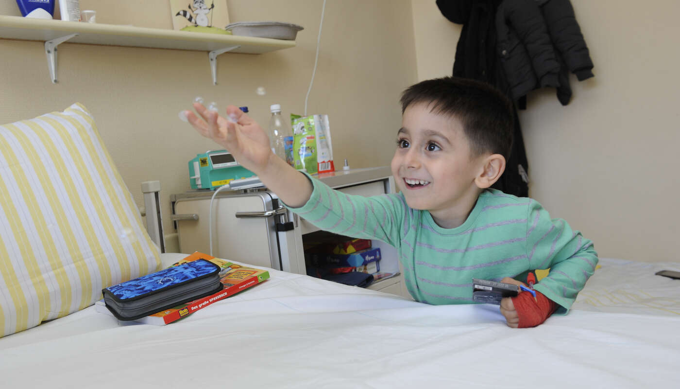 Ein kleiner Junge mit einem Verband am Arm streckt seine Hand aus und lächelt.