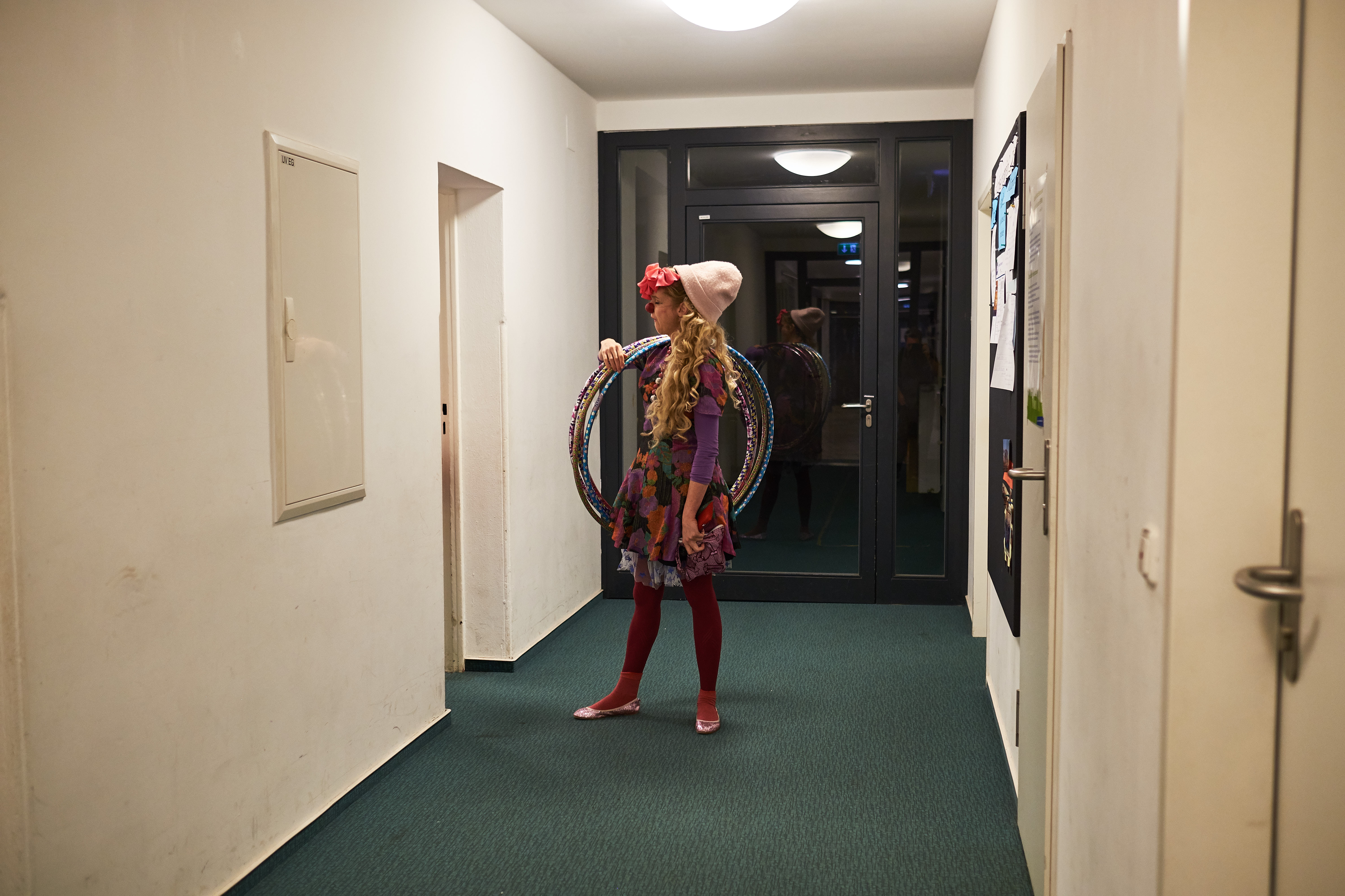 Clown Perdita steht mit Hullahoop Reifen in einem leeren Flur.