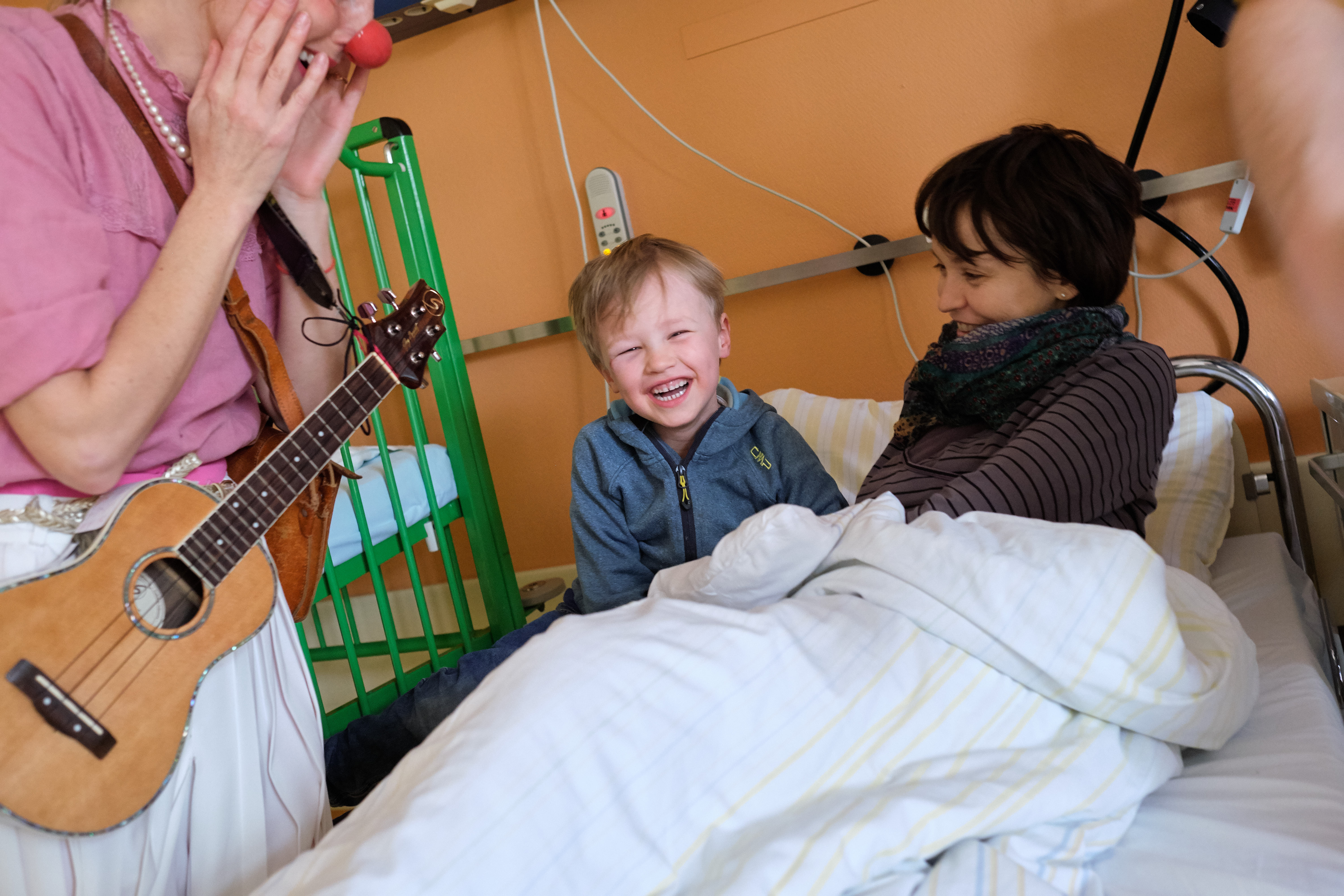 Ein Kind sitzt bei seiner Mama im Krankenhausbett und lacht.